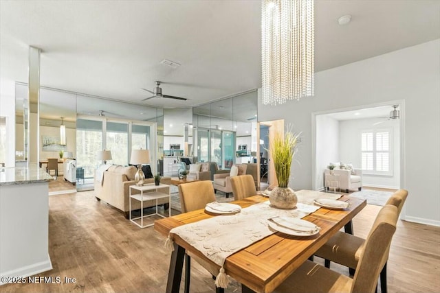 dining room featuring light wood-style flooring, a ceiling fan, visible vents, and baseboards