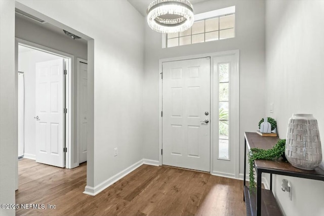 foyer with a healthy amount of sunlight, an inviting chandelier, baseboards, and wood finished floors