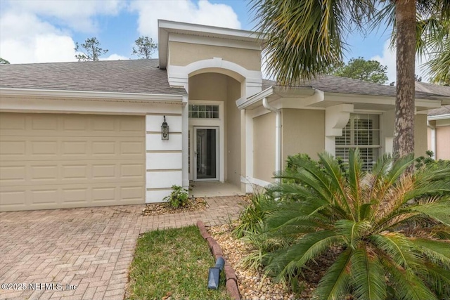 property entrance featuring decorative driveway, roof with shingles, and stucco siding