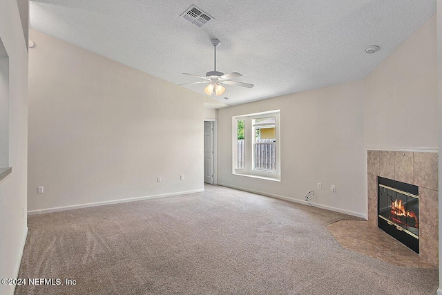 unfurnished living room with ceiling fan, carpet flooring, a tiled fireplace, and a textured ceiling