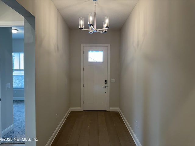 doorway featuring a notable chandelier, dark wood-type flooring, and baseboards