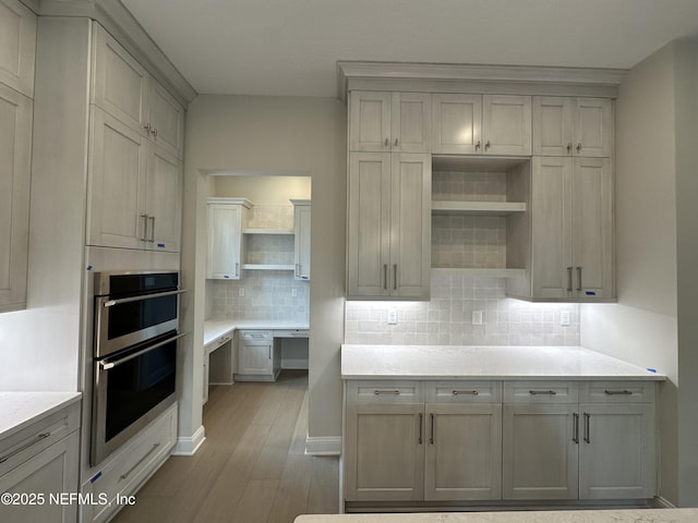 kitchen featuring open shelves, tasteful backsplash, light stone countertops, double oven, and wood finished floors