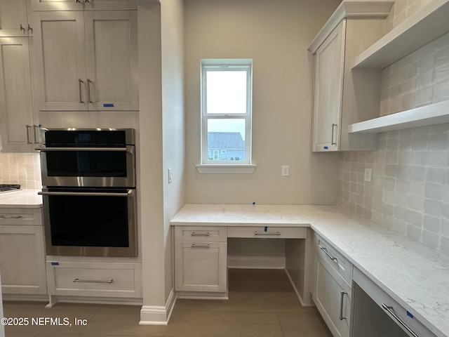 kitchen with double oven, tasteful backsplash, built in study area, and light stone countertops