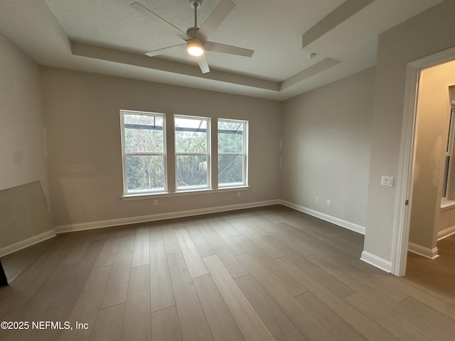 spare room with dark wood-style floors, ceiling fan, a raised ceiling, and baseboards