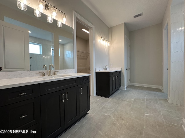 bathroom with a walk in closet, visible vents, two vanities, and a sink