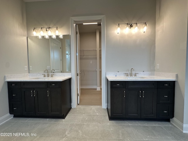 bathroom featuring a spacious closet, two vanities, a sink, and baseboards