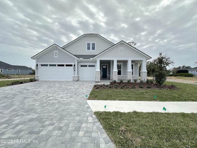 craftsman inspired home with a garage, stone siding, covered porch, decorative driveway, and a front lawn