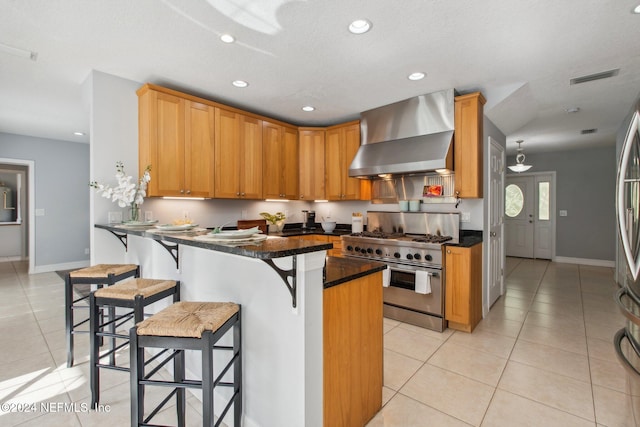 kitchen featuring wall chimney range hood, light tile patterned flooring, a textured ceiling, kitchen peninsula, and high end stainless steel range