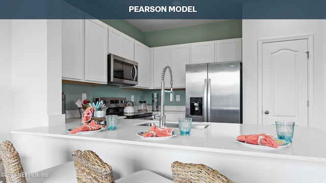 kitchen featuring stainless steel appliances, kitchen peninsula, a breakfast bar area, and white cabinetry