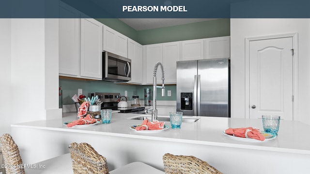 kitchen featuring a sink, light countertops, white cabinets, a peninsula, and appliances with stainless steel finishes
