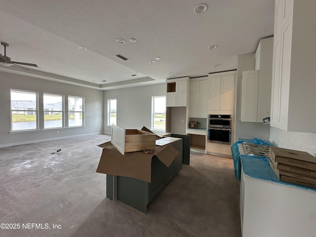 kitchen featuring a textured ceiling, a tray ceiling, stainless steel double oven, white cabinets, and a center island