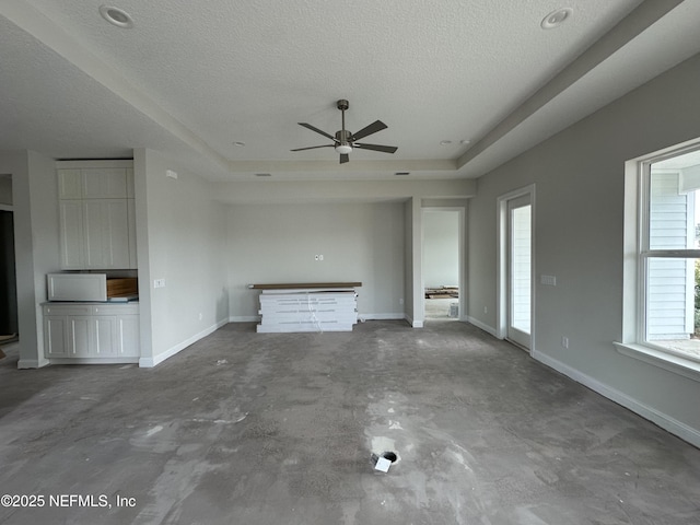 unfurnished living room with a textured ceiling, a tray ceiling, and a wealth of natural light