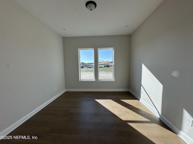 empty room featuring baseboards and dark wood finished floors