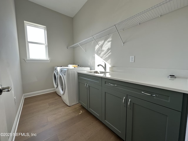 laundry area with washing machine and dryer, a sink, baseboards, cabinet space, and light wood finished floors