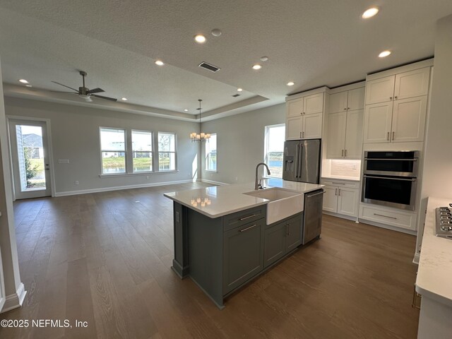 kitchen featuring visible vents, a raised ceiling, appliances with stainless steel finishes, light countertops, and a sink