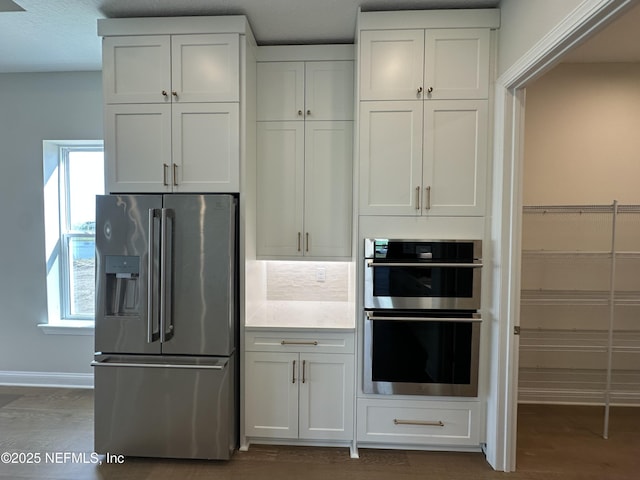 kitchen with stainless steel appliances, white cabinets, baseboards, and dark wood-style floors