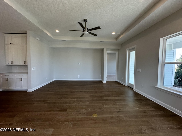 unfurnished living room featuring a raised ceiling, dark wood finished floors, a textured ceiling, and baseboards