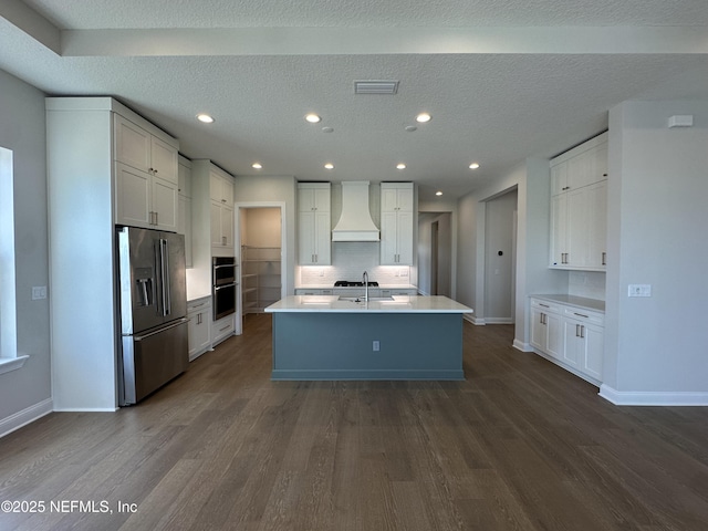 kitchen with visible vents, dark wood-type flooring, custom exhaust hood, stainless steel appliances, and a sink