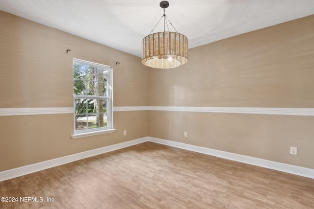 empty room featuring wood-type flooring and a notable chandelier