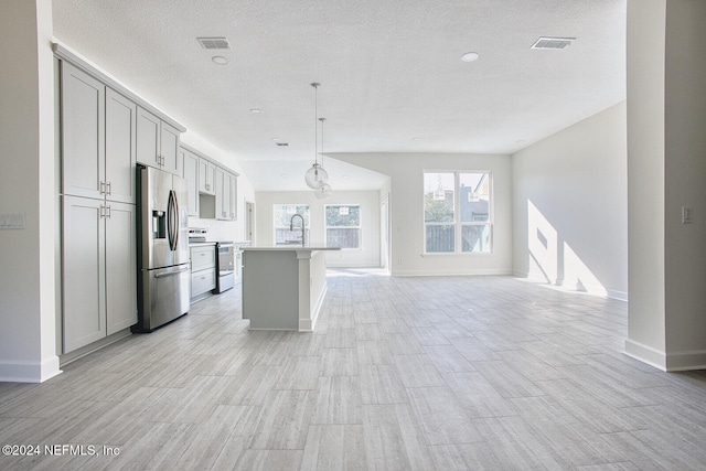 kitchen with an island with sink, gray cabinetry, light hardwood / wood-style floors, hanging light fixtures, and appliances with stainless steel finishes