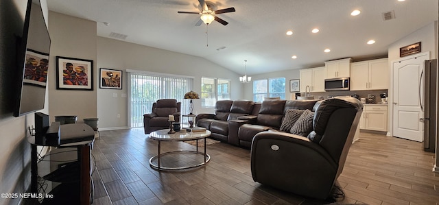 living room featuring vaulted ceiling, ceiling fan with notable chandelier, and light wood-type flooring