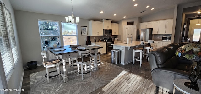 kitchen with pendant lighting, white cabinetry, appliances with stainless steel finishes, and a kitchen island with sink