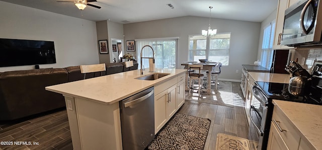 kitchen featuring lofted ceiling, sink, decorative light fixtures, appliances with stainless steel finishes, and an island with sink