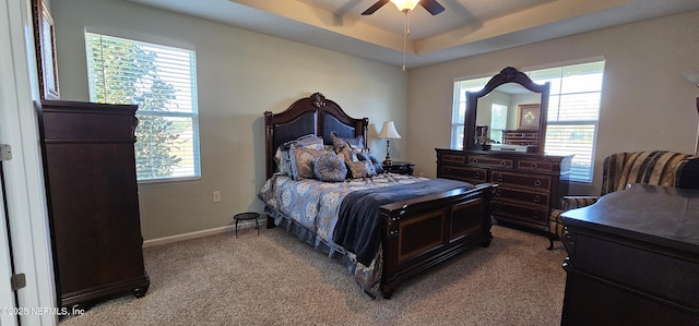 carpeted bedroom with multiple windows, a tray ceiling, and ceiling fan