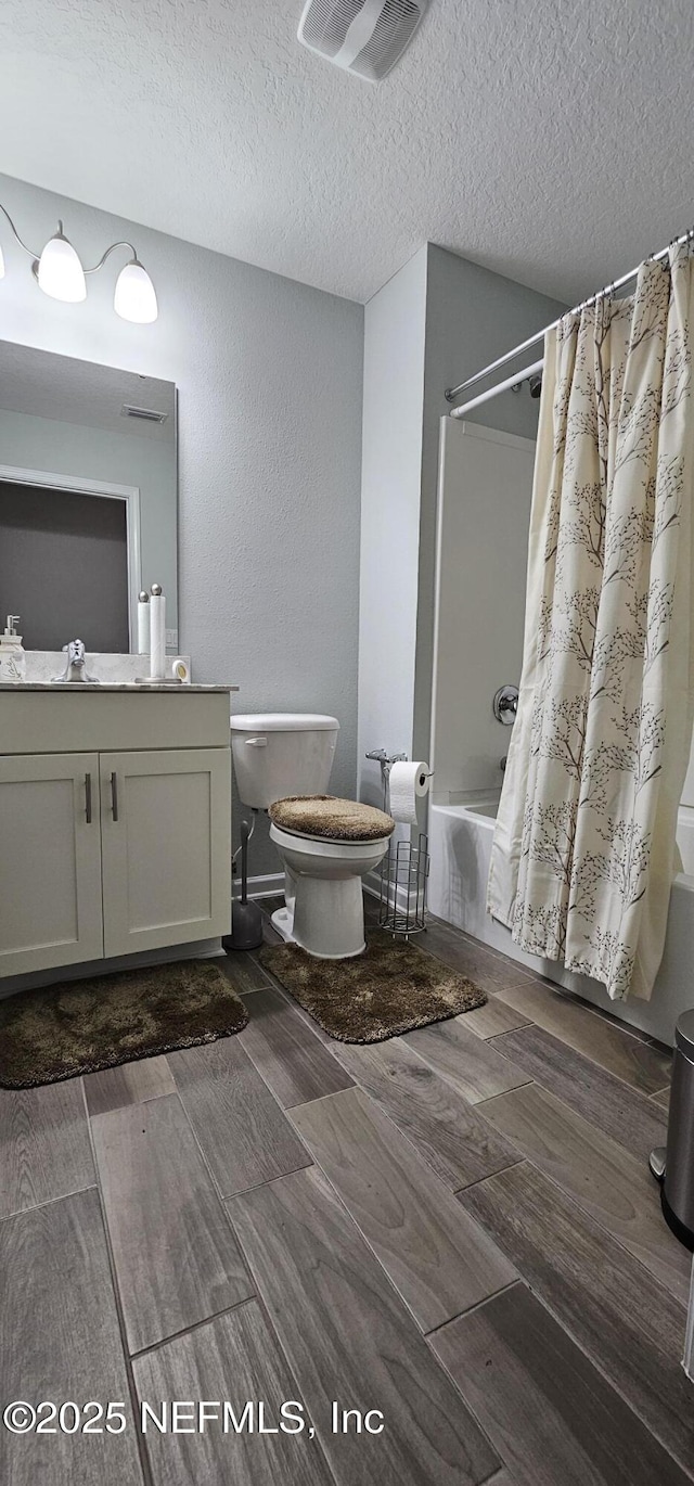 full bathroom featuring shower / bath combination with curtain, vanity, toilet, and a textured ceiling