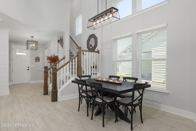 dining room with a high ceiling, light hardwood / wood-style flooring, plenty of natural light, and an inviting chandelier