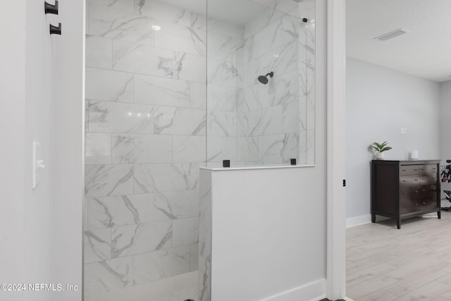 bathroom with a tile shower and wood-type flooring