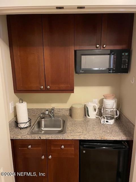 kitchen with light stone countertops, black appliances, and sink