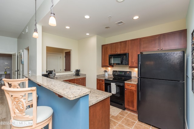 kitchen with kitchen peninsula, black appliances, a kitchen bar, pendant lighting, and light stone counters