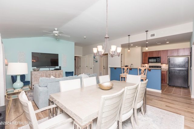 dining space with ceiling fan with notable chandelier, light wood-type flooring, and vaulted ceiling