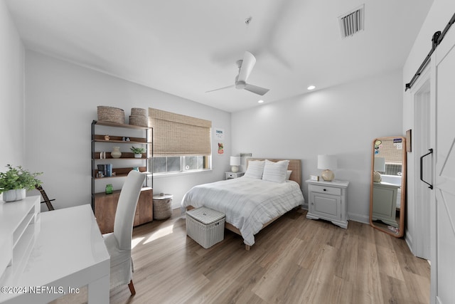 bedroom with a barn door, a closet, light hardwood / wood-style flooring, and ceiling fan