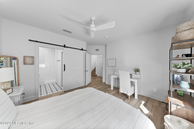 bedroom featuring ensuite bathroom, light wood-type flooring, ceiling fan, and a barn door