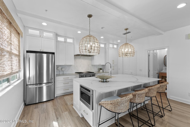 kitchen with an island with sink, stainless steel appliances, white cabinets, sink, and a notable chandelier