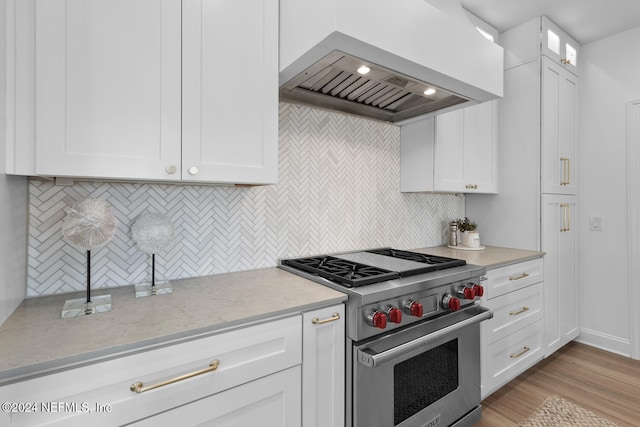 kitchen with white cabinets, tasteful backsplash, wall chimney exhaust hood, designer stove, and light hardwood / wood-style floors