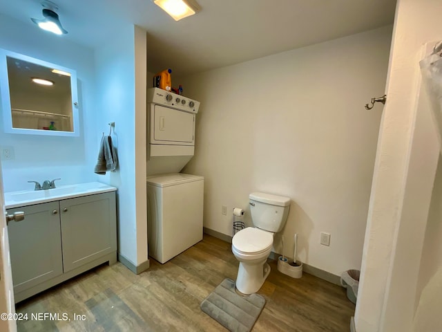 bathroom with wood-type flooring, stacked washer and dryer, vanity, and toilet