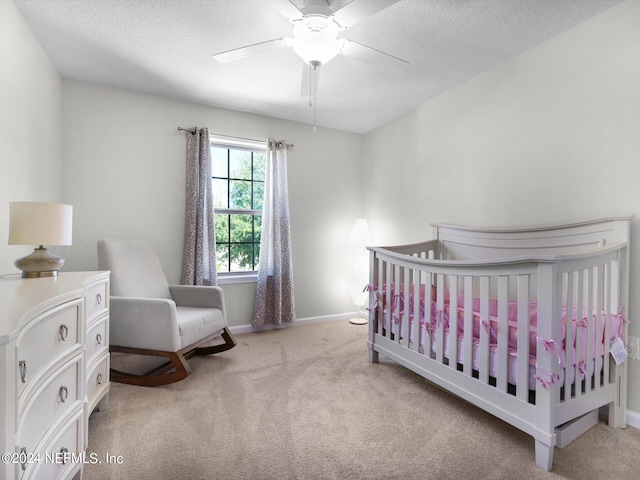 bedroom with a textured ceiling, light colored carpet, a crib, and ceiling fan