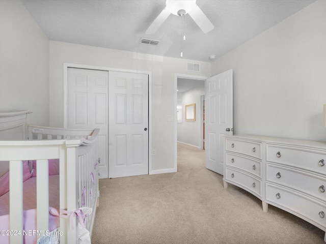 bedroom with a textured ceiling, light colored carpet, a closet, and ceiling fan