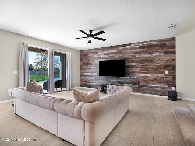 living room with a textured ceiling, wooden walls, light wood-type flooring, and ceiling fan