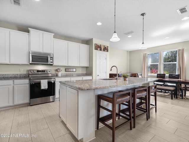 kitchen with an island with sink, sink, pendant lighting, white cabinetry, and appliances with stainless steel finishes