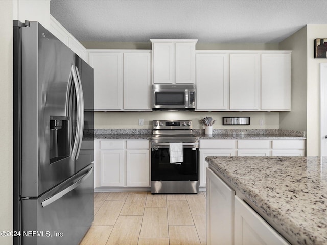 kitchen featuring white cabinets, light stone countertops, stainless steel appliances, and a textured ceiling