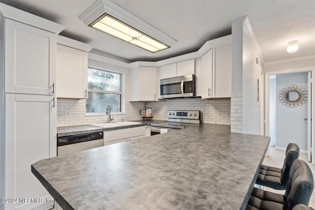 kitchen with kitchen peninsula, stainless steel appliances, white cabinets, ornamental molding, and a breakfast bar area