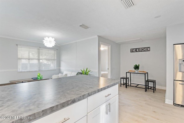 kitchen with stainless steel fridge, white cabinets, light wood-type flooring, and ornamental molding