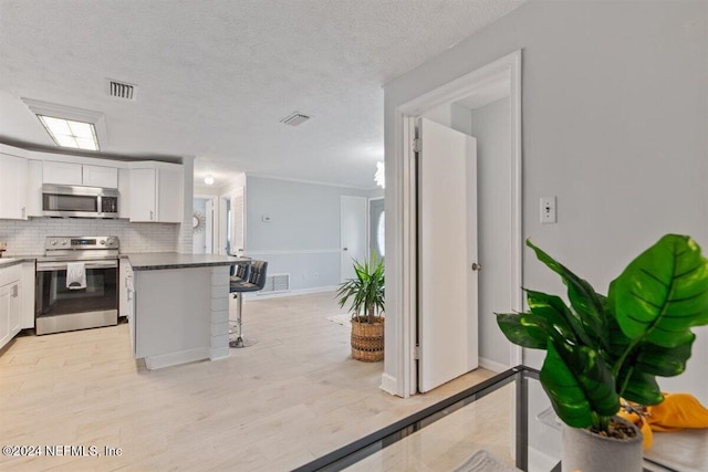 kitchen featuring decorative backsplash, appliances with stainless steel finishes, a breakfast bar, white cabinetry, and light hardwood / wood-style flooring