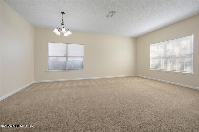 carpeted empty room with a notable chandelier and a textured ceiling