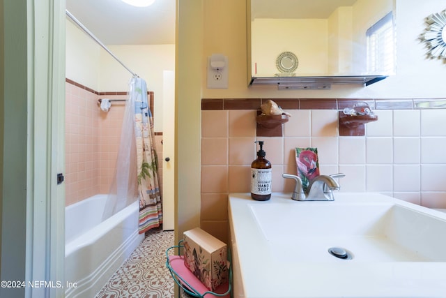 bathroom featuring tile walls, shower / bath combo with shower curtain, and sink