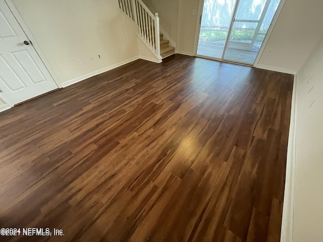 unfurnished living room featuring dark wood-style flooring, stairway, and baseboards